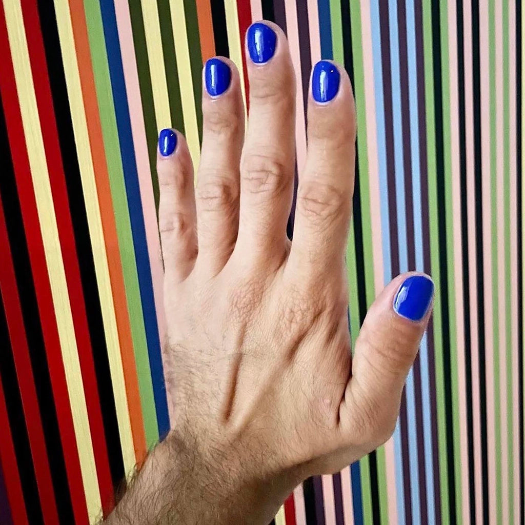 To Be Frank cobalt blue nail polish named Evil Eye painted on man's hand against colorful background